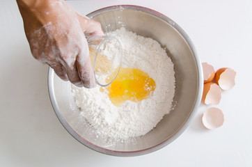 Hand pouring sugar and egg yolk mixing with flour to making bread or cake,bakery cooking