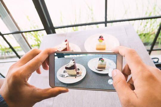 Hand holding smartphone and taking photo of delicious cake