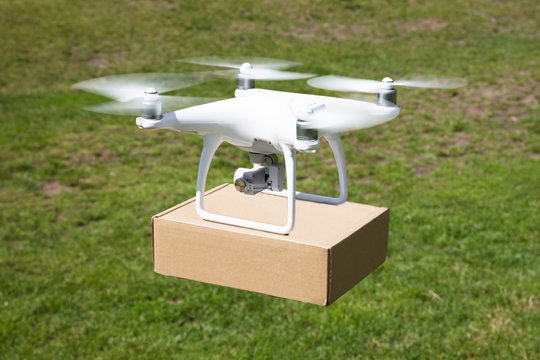 Drone Carrying Parcel Over Grassy Field