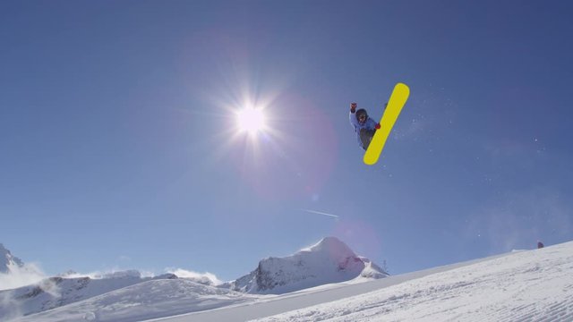 SLOW MOTION: Young pro snowboarder riding the half pipe in big mountain snow park, jumping high out of the halfpipe wall, performing tricks and rotations with grabs in sunny winter 