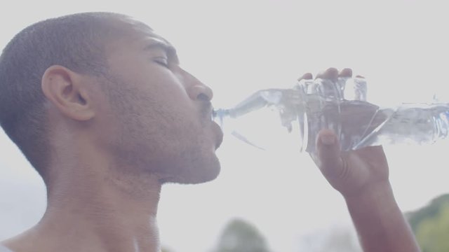Young adult male drinking water in the bright sunshine as he talks, in slow motion