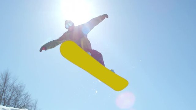 SLOW MOTION: Extreme snowboarder man riding in sunny mountain snow park and jumping over big air kicker in sunny winter. Young pro snowboarder jumping over the sun