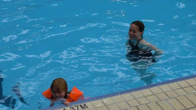 A mother and daughter swim together in an indoor pool.