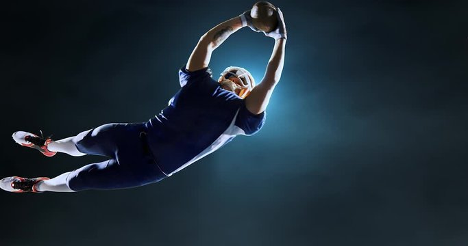 American football player jumps with a ball on a dark background