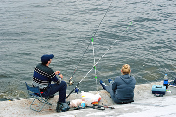 the couple sitting on the pier with a fishing rod