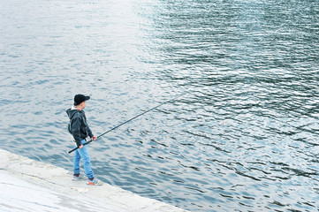 a lone boy stands on a pier with a fishing rod