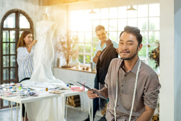 Young handsome asian confident fashion designer-clothes man with tablet pc and team are working at studio. Happy work for successful . Teamwork fashion designer concept