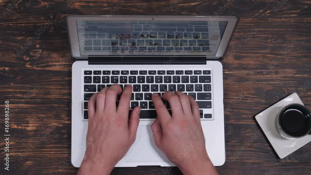 Poster unrtop view male hands typing on computer. working place with wooden desk cup with coffee and laptop