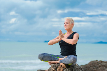 Beautiful mature aged woman doing yoga on a desert tropical beach