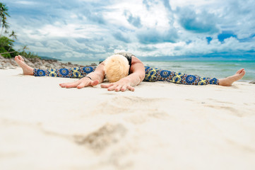 Beautiful mature aged woman doing yoga on a desert tropical beach