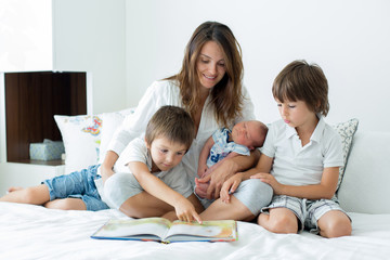 Obraz premium Young mother, read a book to her three children, boys, in the bedroom
