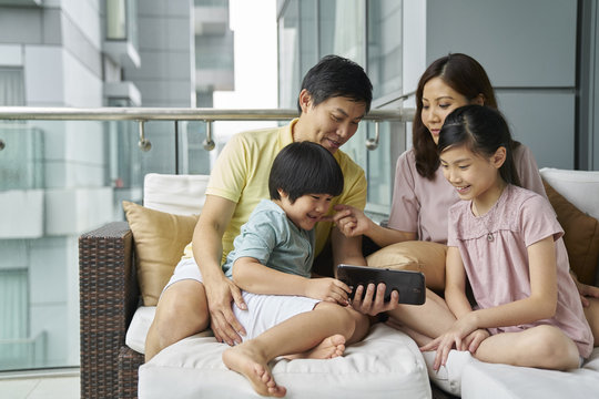 Family of four bonding on the balcony over an electronic tablet
