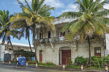 Street with an old building, green palms and a ricksha on the road, Toamasina, Madagascar
