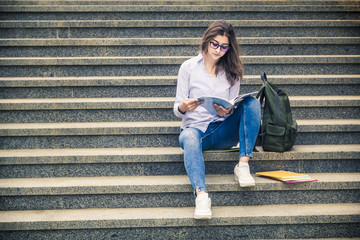A girl is reading a book on the stairs.