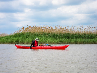 Man in red kayak in red life jacket kayaking in wild Danube river near confluence of the Danube in the Black sea