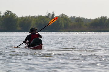 Fototapeta na wymiar Man in red kayak in red life jacket kayaking in wild Danube river on biosphere reserve in spring