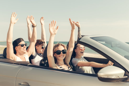 Smiling friends driving car near the sea and having fun