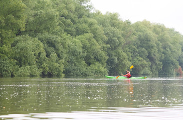 Girl in green kayak kayaking in wild Danube river on biosphere reserve in spring