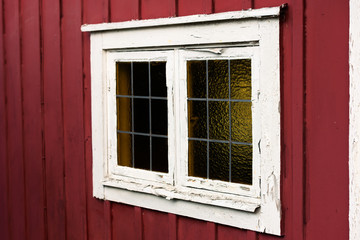 Fototapeta premium Stare okno na czerwony domek z białą ramą okienną. Biała ramka łuszczy się i wymaga uwagi. Ołów szprosy lub listwy przyszybowe na szybie.