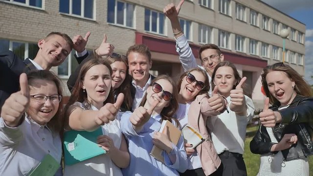 Happy students on the background of his school raises his hands with a finger up. Demonstrate the success and good mood and graduation.