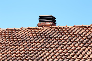 Typical tiled roof and chimney against blue sky