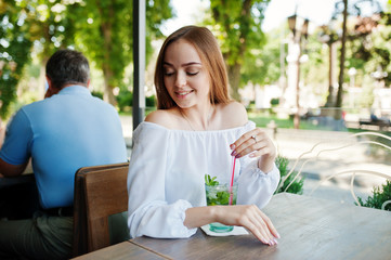 Portrait of a stunning young woman posing with mojito cocktail in cafe next to the park.