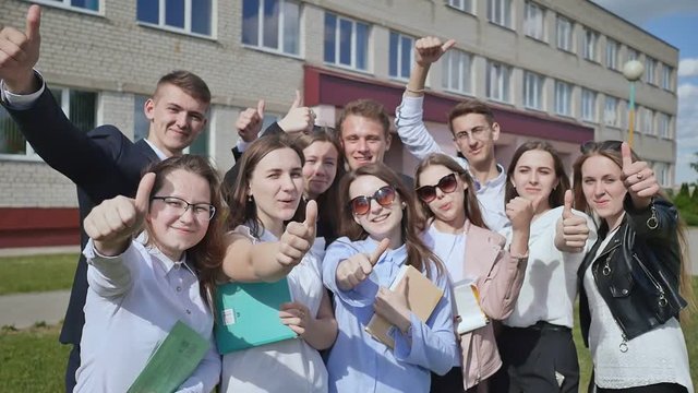 Happy students on the background of his school raises his hands with a finger up. Demonstrate the success and good mood and graduation.