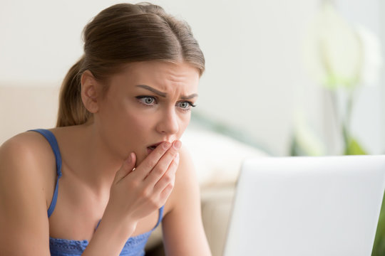 Upset young woman looking on laptop screen with fear. Lady with worried face watching horror movie, reading sad e-mail message, shocked of bad news in Internet, surprised with TV-show plot scary twist