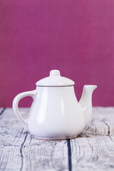 en vit porslins te kanna på trä bord med lila bakgrund
