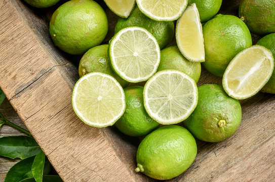Fresh green lime with some slices and cut pieces on wooden tray background.