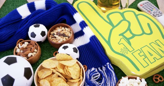 Bowl of snacks, football, beer, foam finger and shawl on artificial grass 