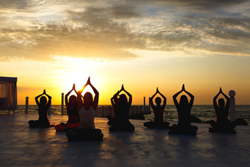A group of women doing yoga at sunrise near the sea