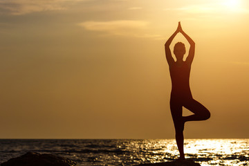 A woman in a red suit practicing yoga on stone at sunrise near the sea