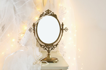 Old vintage oval mirror and beautiful white wedding dress and veil on chair with gold garland lights
