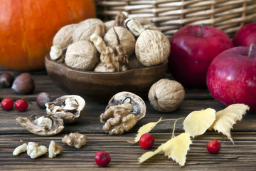 Small pumpkins, nuts, apples and berries of mountain ash with autumn leaves on rustic wooden background. Autumn concept, decor, a place for your text. Background, top view