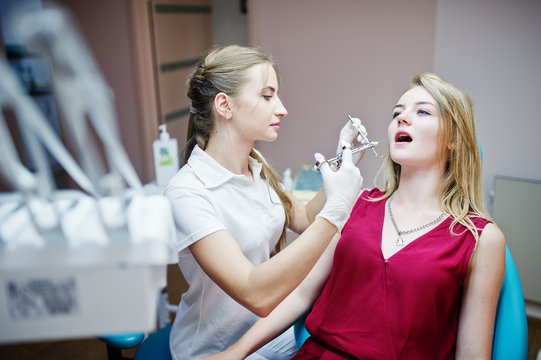Attractive female orthodontist injecting anesthesia to her patient in a red-violet dress.