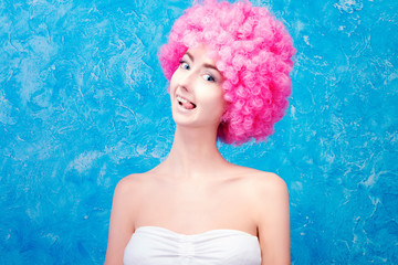 Alone comic female / woman / girl with pink curved wig on blue background with cheeky emotion. Clown concept