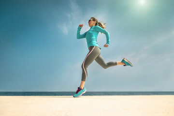 Woman running along the sealine coast under sunlight at sunny su