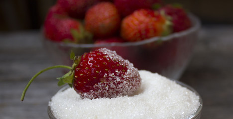 Strawberries in white bowl with granulated sugar on vintage wooden board.