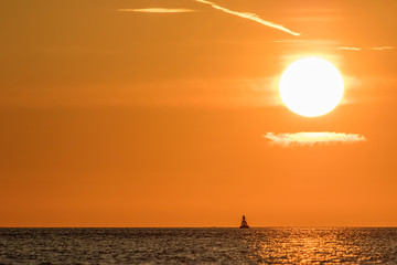 Zen sky. Beautiful sunrise with clear orange sky above calm sea and solitary buddha shaped buoy.
