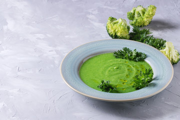 Vegetarian vegan broccoli cream soup served in blue plate with fresh parsley and broccoli over gray concrete background. Copy space. Healthy eating.