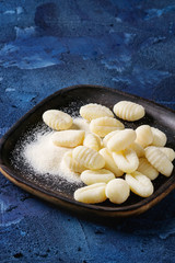 Raw uncooked potato gnocchi in black wooden plates with flour over dark blue concrete background. Close up with space. Home cooking.