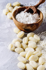 Raw uncooked potato gnocchi with olive wood bowl of flour, grated parmesan cheese over gray concrete background. Close up with copy space. Home cooking.