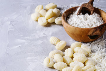 Raw uncooked potato gnocchi with olive wood bowl of flour, grated parmesan cheese over gray concrete background. Close up with copy space. Home cooking.