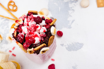 Vanilla and raspberry extreme milkshakes with pretzels, popcorn, small marshmallows, cookies and berries on white background. Copy space