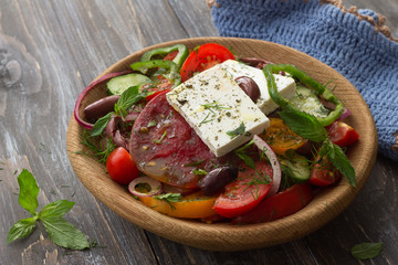 Homemade Greek salad from tomatoes, cucumbers, sweet peppers, cheese, olives and greens in a wooden bowl on a wooden table. Healthy delicious food
