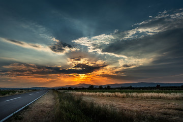 Naklejka na ściany i meble Highway Road at sunset with fields and dramatic cloudscape