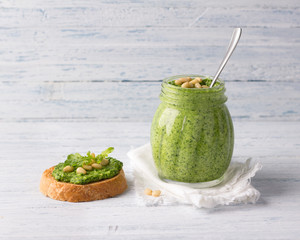 Fresh homemade pesto sauce from arugula with pine nuts in a glass jar on a blue wooden background. Delicious healthy food. Selective focus - obrazy, fototapety, plakaty
