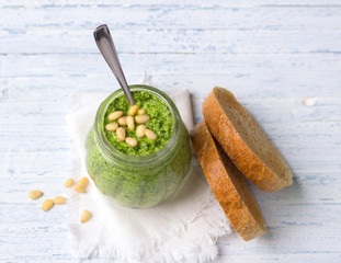 Fresh homemade pesto sauce from arugula with pine nuts in a glass jar on a blue wooden background....