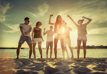 Friends funny dance on the beach under sunset sunlight.